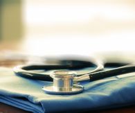 Stethoscope with blue doctor coat on wooden table with shallow DOF eve